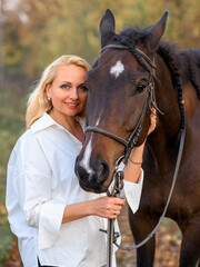 Fototapeta premium beautiful caucasian girl in a white shirt with a horse in the forest at sunset