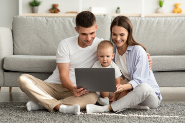 Fototapeta premium Happy Young Parents And Their Toddler Baby Using Laptop Together At Home
