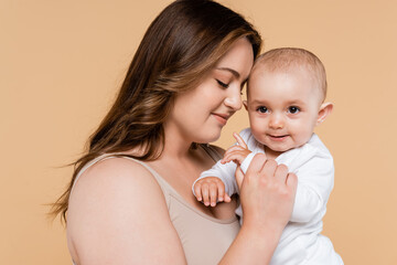 Brunette woman with closed eyes holding baby isolated on beige.