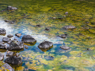 Beautiful nature background of stony bottom in turquoise transparent water. Glowing green natural background with a swamp surface. Scenery with wild flora of highlands in swampy mountain lake.