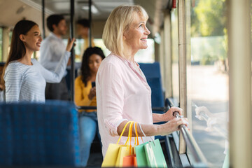 Smiling mature woman taking bus, holding shopping bags