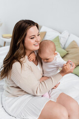 Happy plus size mother hugging baby girl on bed at home.