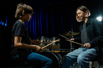 Young woman teaching boy to play drums.