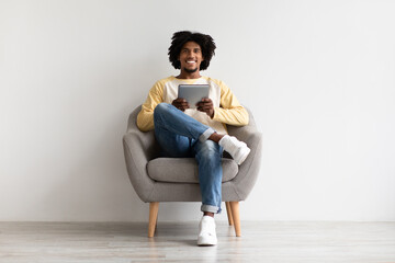 Cheerful Young Black Man Relaxing In Chair With Digital Tablet