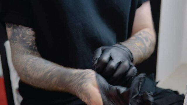 Tattoo master with tattooed hands wears sterile gloves and disinfects his hands before working with the client. Observance of sanitary norms and prevention of hepatitis and AIDS during tattooing