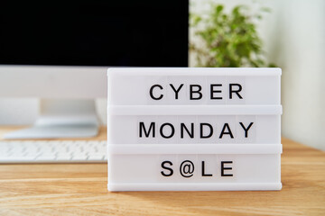 Cyber monday sale is written on a light box. The light box is on a wooden desk. Computer in background blurred. Cyber monday week concept.