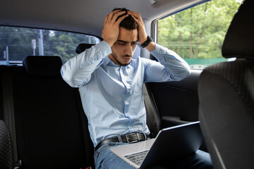 Worried middle eastern businessman using laptop in car