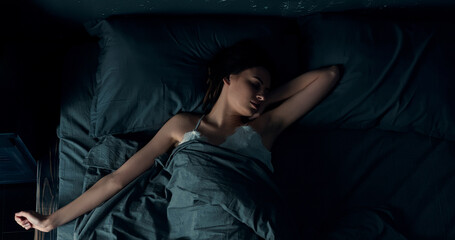 Brunette woman lying sound asleep in bed, changing position. A young caucasian lady is about to awake, stretching her arms while sleeping.