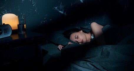 Beautiful young brunette woman sleeping on side, lying cozily in bed, hugging a pillow. Lady sound asleep at night. Loft interior.