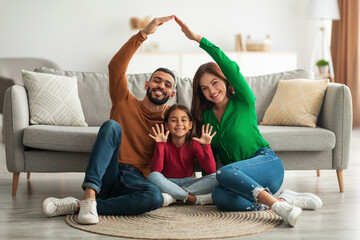 Cheerful parents making symbolic roof of hands above their daughter