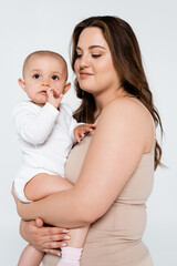 Smiling mother with overweight hugging baby girl isolated on grey.
