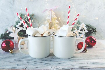 Obraz na płótnie Canvas Cups of coffee with marshmallows, fir branches, Christmas decorations and illumination on a wooden table, the concept of celebration, home comfort, congratulations, Happy New Year 