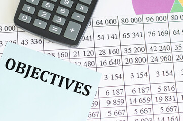 text OBJECTIVES on a card against the background of accounting reports next to the calculator