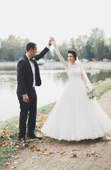 Stylish couple of happy newlyweds walking in the park on their wedding day with bouquet