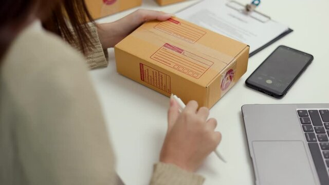 Close up shot business woman hand writing address to sending product to customer using smartphone scan qr code on the box. Online business working at home. Startup Small business owner entrepreneur