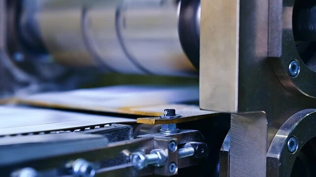 Strong bolts and internal screws holding a construction of a machine for producing diapers. A large rotating horizontal shaft over the conveyer belt blurred at the backdrop..