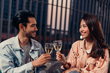 Portrait of Happy Asian young couple hand holding glasses of champagne having romantic dating at night on Valentine's day or anniversary, woman smile with love to boyfriend