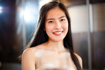 Portrait of attractive beautiful Asian woman holding glasses of wine or beer alcohol toasting to camera, focus on female happy smile face, lifestyle party music with light at night on rooftop 