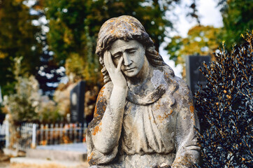 Old stone statue in the cemetery. Sad stone woman.