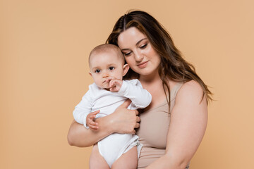 Young mother with overweight holding baby isolated on beige.