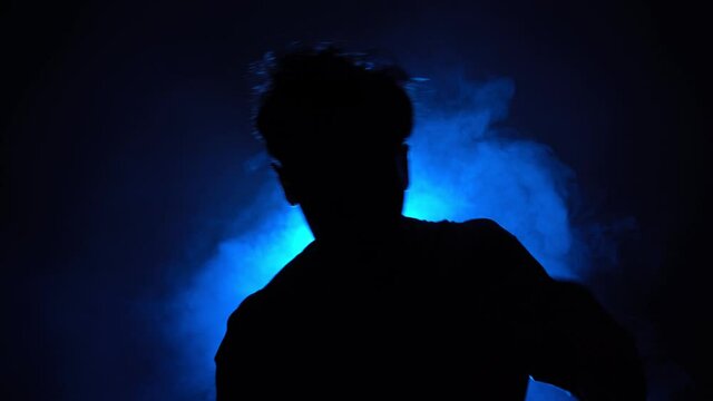 Silhouette, man street dancer dancing stylish dance in a smoky room with backing blue neon light. Club party.