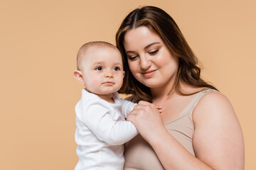 Smiling woman with overweight holding baby daughter isolated on beige.