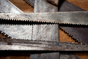 Old vintage metal saws for wood of different shapes and sizes, crumpled on a wooden background.
