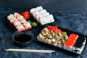 Sushi rolls with mussels, caviar, wasabi, ginger, cheese, shrimp, chicken, soy sauce and cucumber in plastic packaging for takeaway on a dark background