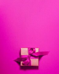 Brown paper gift box with a purple satin ribbon bow on top on purple background. Christmas holiday mother and father Valentines days and birthday present flat lay concept with copy space.