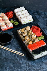 Sushi rolls with mussels, caviar, wasabi, ginger, cheese, shrimp, chicken, soy sauce and cucumber in plastic packaging for takeaway on a dark background