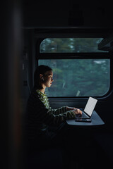 Beautiful woman working in the evening in the train on a laptop with a serious face. Work on the go.