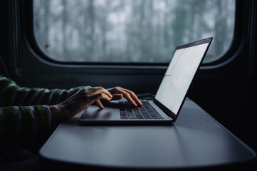 Close photo, woman working in the evening at the table in the train, typing text on laptop keyboard on the background of the window with evening views