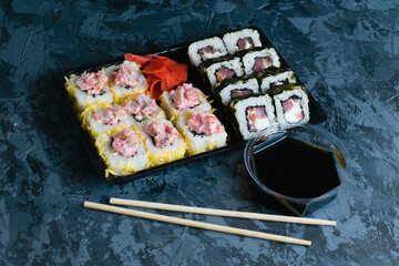Delicious sushi with soy sauce, fish, cheese, caviar, wasabi and ginger in plastic packaging for takeaway on a dark background