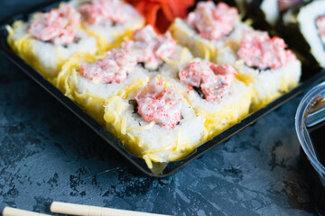 Delicious sushi with soy sauce, fish, cheese, caviar, wasabi and ginger in plastic packaging for takeaway on a dark background