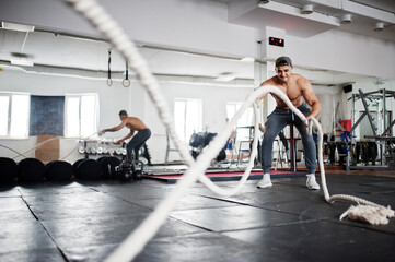 Fit and muscular arabian man working out with heavy ropes in gym.