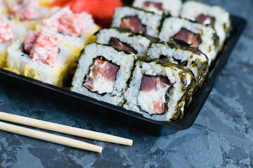 Delicious sushi with soy sauce, fish, cheese, caviar, wasabi and ginger in plastic packaging for takeaway on a dark background