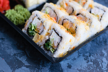 Delicious sushi rolls with fish, nori and chicken in plastic packaging for takeaway on a dark background