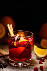 Glass of hot red mulled wine with orange slice and spices of star anise and cinnamon on a wooden table.