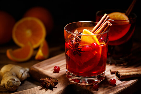 Glass of hot red mulled wine with orange slice and spices of star anise and cinnamon on a wooden table.
