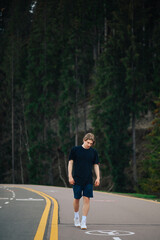 Man walks on a mountain road against the backdrop of coniferous trees. Vertical photo of a male tourist on a walk.