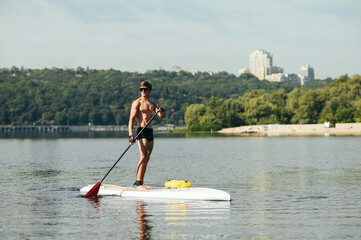 Athlete with an athletic body with an oar in his hands stands on a sup board and looks to the side...