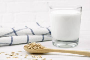 Oatmeal in a wooden spoon, a glass of milk and tea towel on light background. Healthy food concept, oat milk, food for allergy sufferers and vegetarians. Selective focus on spoon, blurred background.