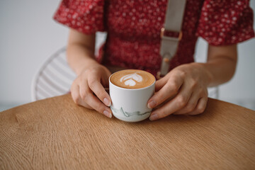 Female hands hold a beautiful cup of aromatic cappuccino or latte coffee on a wood table in a morning cafe