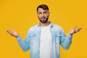 Pensive confused handsome adult european guy with beard spreads his arms to sides