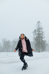 Fototapeta na wymiar Full-length portrait of a stylish lady in casual clothes on a walk on a snowy winter day, having fun in the snowfall with a smile on her face.