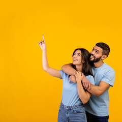 Good offer. Portrait of arab couple hugging, looking and pointing at copy space on yellow background, crop