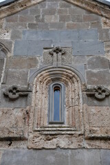 Fototapeta na wymiar A narrow small window in the wall of an old stone house. Carved stone window.