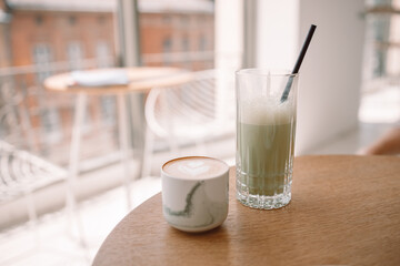 Cappuccino coffee and iced green matcha latte tea in ceramic mug on wooden table at modern style cafe. Tasty morning drinks.