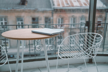White loft restaurant interior with dining table, chairs on a sunny summer day. Fashion magazine on wood table