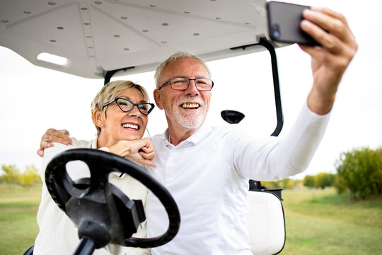 Happy senior couple in golf buggy taking a photo before recreation and enjoy free time outdoors.